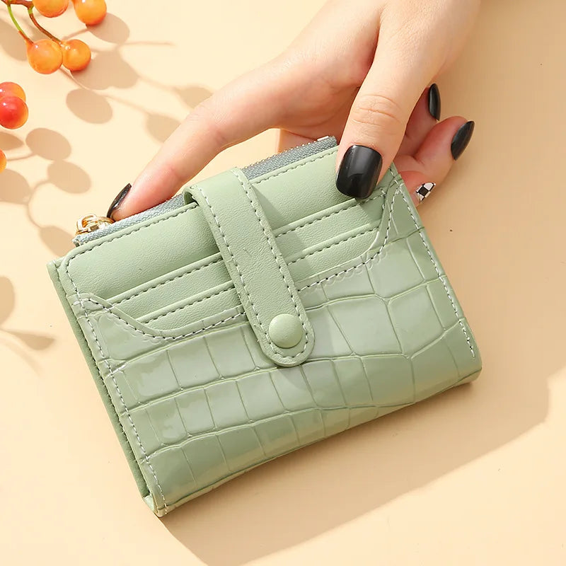 Light green wallet with crocodile texture held by a hand on a beige background