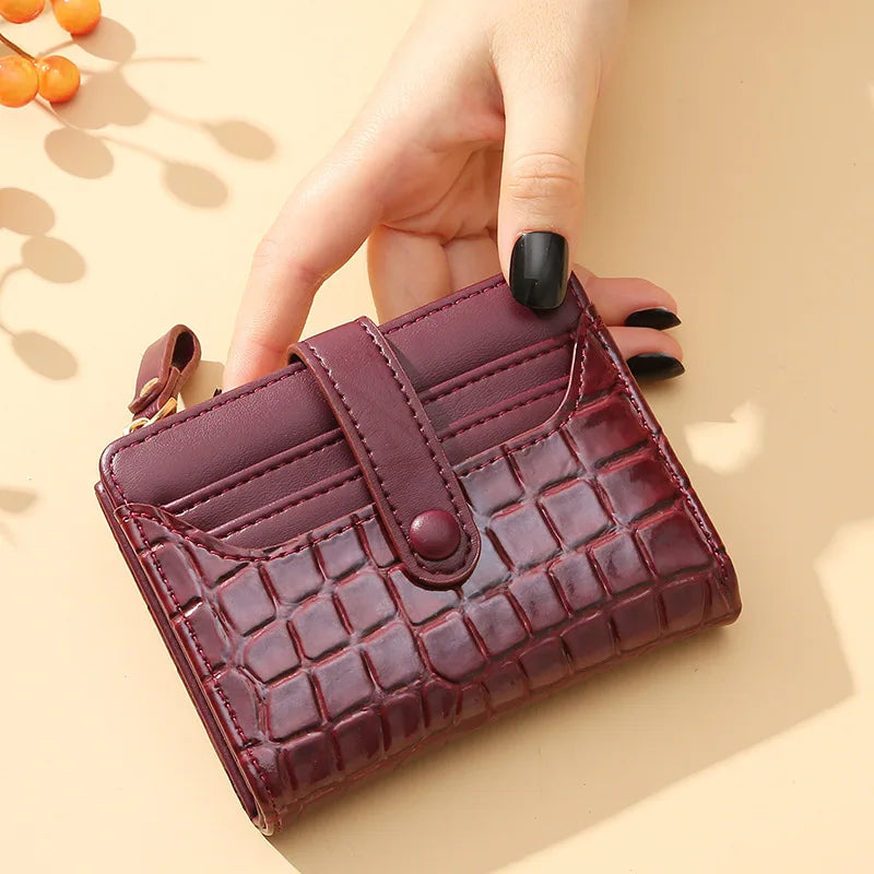 Hand holding a maroon textured wallet on a beige background