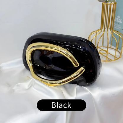 Black and gold Carauana Festival Clutch Bag on a white surface with a blurred background