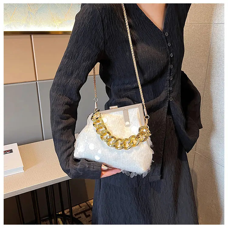 Person holding a white handbag with gold chain detail indoors.