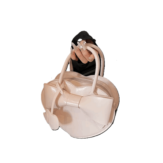 Beige handbag with bow detail held by a hand against a white background