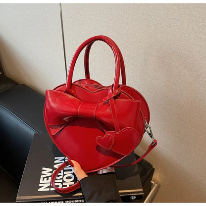Red heart-shaped carauana-lovely-shoulder-bag-heart with a bow on top, held by a person against a neutral background.